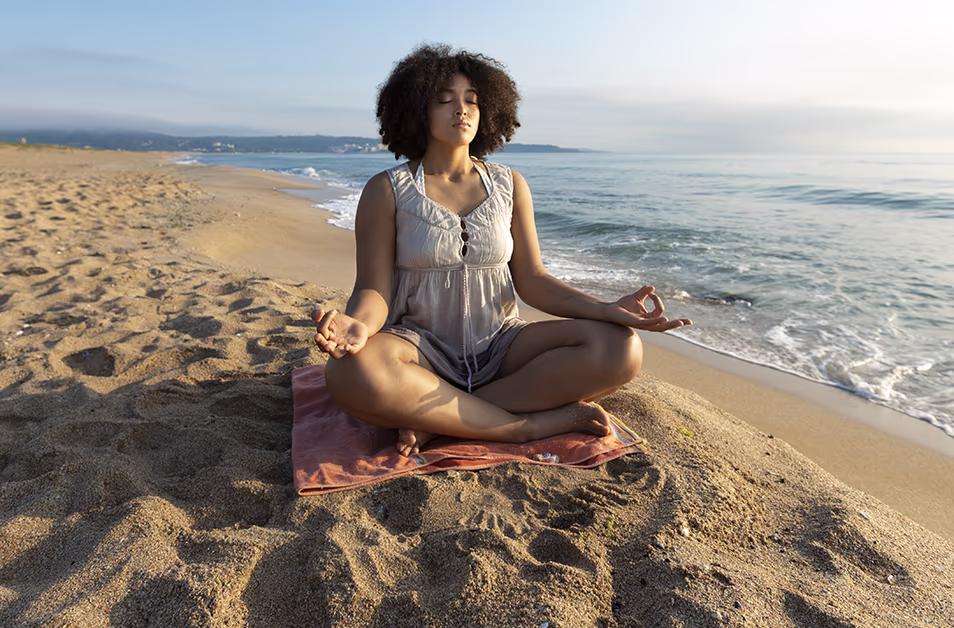 Three people meditate on the beach during a wellness travel retreat