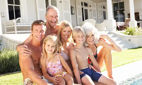 A family with grandparents, parents, and kids sitting in the pool at a luxury villa.